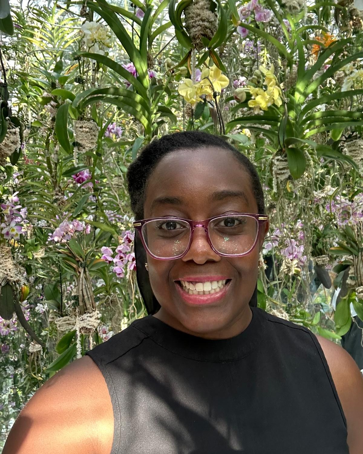 Dr. Keri smiling in front of a wall of hanging orchids.
