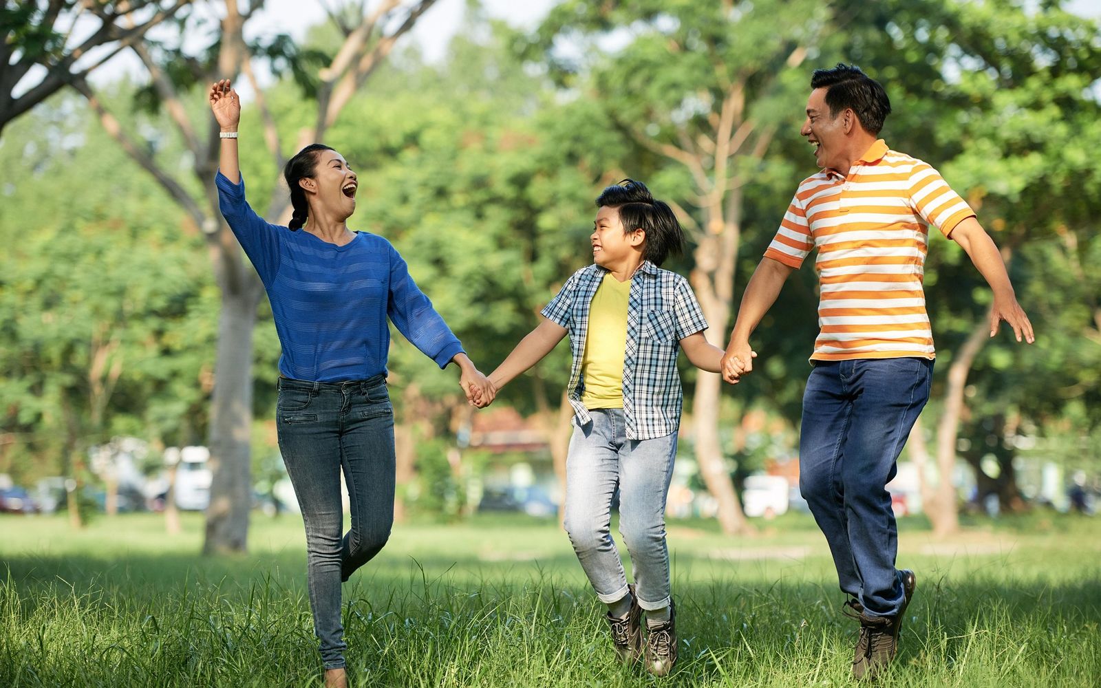 A mother, father, and child running hand in hand through a park, all three laughing.