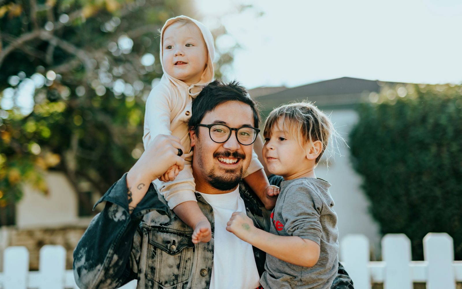 A father laughing with his toddler on his shoulders and his young son in his arms.