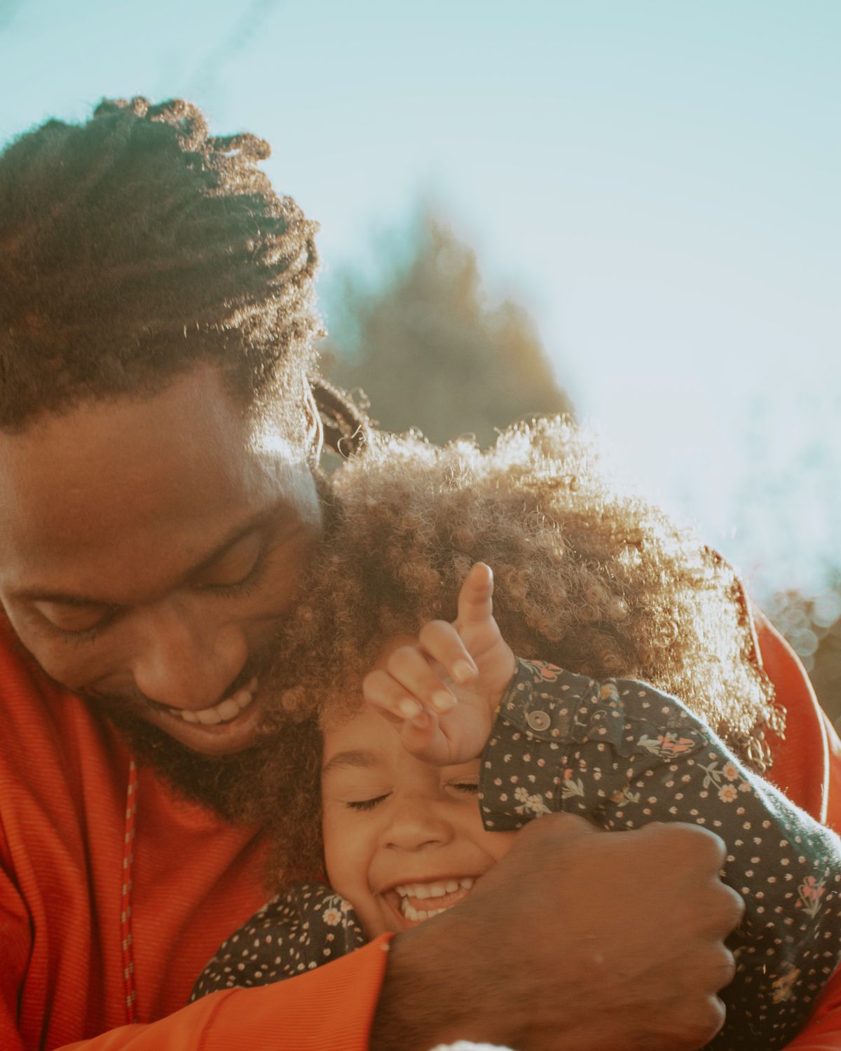 A father hugging his laughing daughter in the sun.